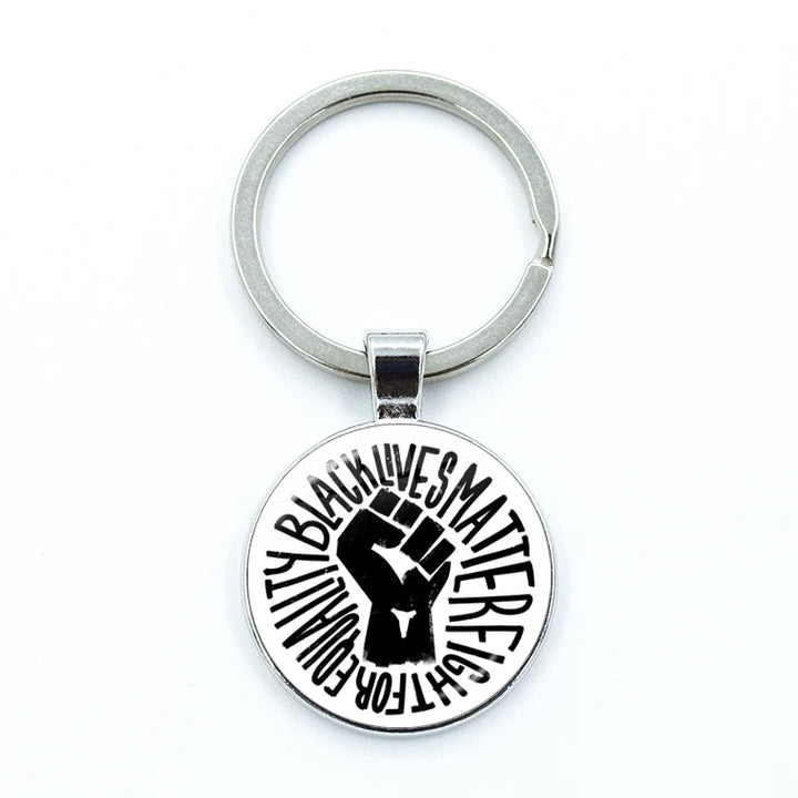 A silver metal keychain featuring a round pendant with a black raised fist graphic and the words 'BLACK LIVES MATTER' and 'EQUALITY' in black lettering on a white background.